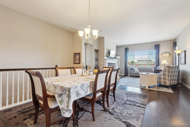 dining space with a chandelier, dark wood-style flooring, a fireplace, and baseboards