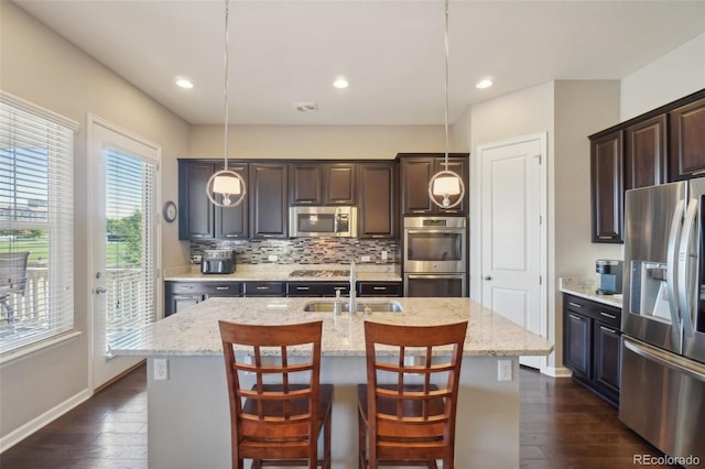 kitchen featuring stainless steel appliances, a sink, dark wood-style floors, an island with sink, and decorative backsplash