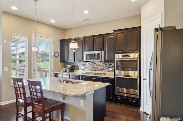 kitchen featuring stainless steel appliances, a sink, dark wood-style flooring, backsplash, and light stone countertops