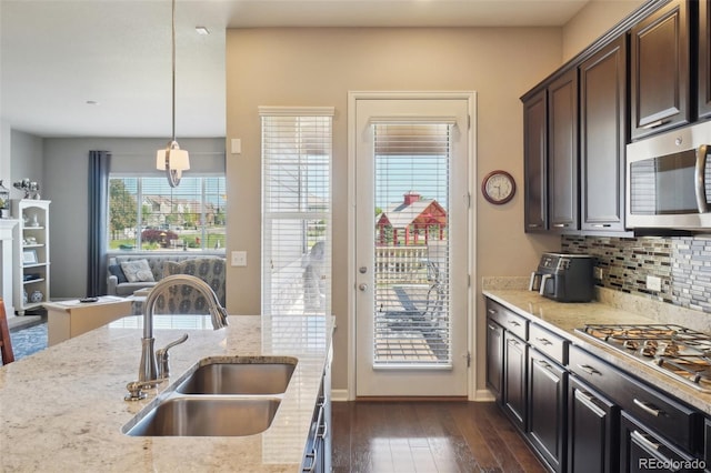 kitchen featuring stainless steel appliances, a sink, dark wood finished floors, backsplash, and light stone countertops