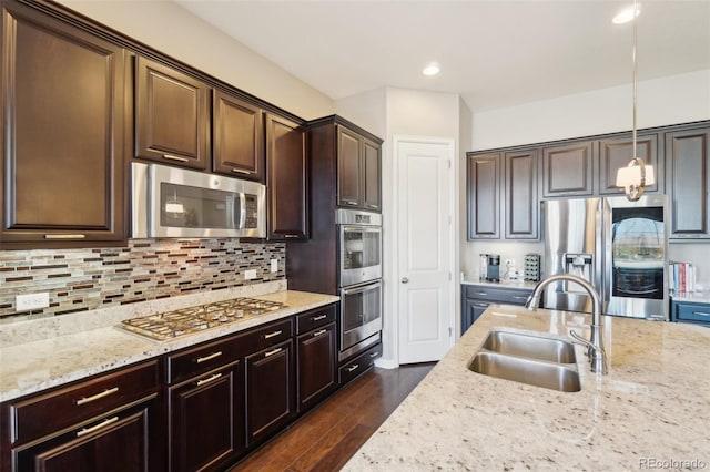 kitchen with stainless steel appliances, a sink, dark brown cabinets, light stone counters, and backsplash