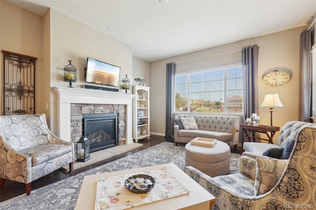 living area with wood finished floors, a stone fireplace, and baseboards