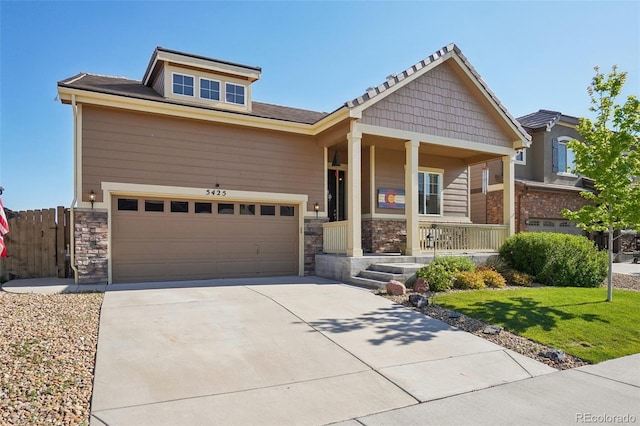 craftsman-style home with a porch, stone siding, driveway, a front lawn, and an attached garage