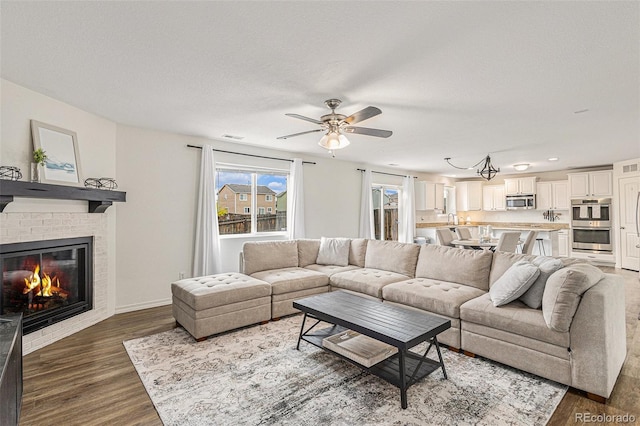 living room with ceiling fan, a fireplace, dark hardwood / wood-style floors, and a textured ceiling