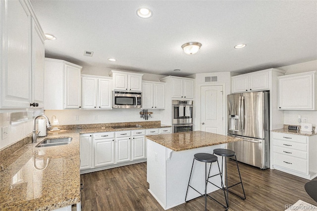 kitchen with sink, white cabinetry, a center island, appliances with stainless steel finishes, and light stone countertops