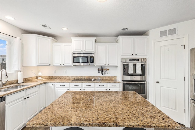 kitchen with stainless steel appliances, white cabinetry, a kitchen island, and sink