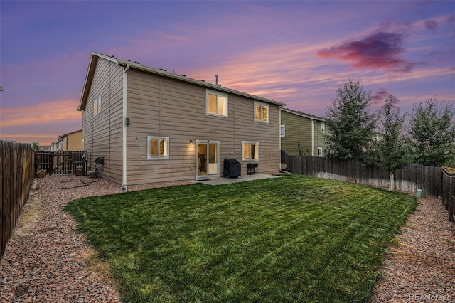 back house at dusk featuring a patio area and a lawn