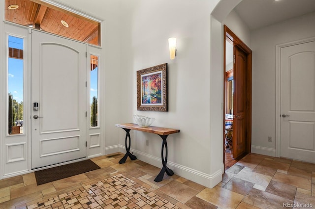 foyer featuring baseboards, arched walkways, and stone tile flooring