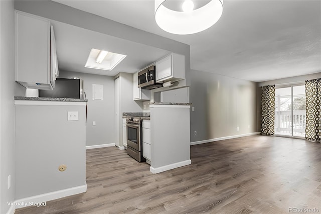 kitchen with a skylight, white cabinets, light wood-type flooring, and appliances with stainless steel finishes