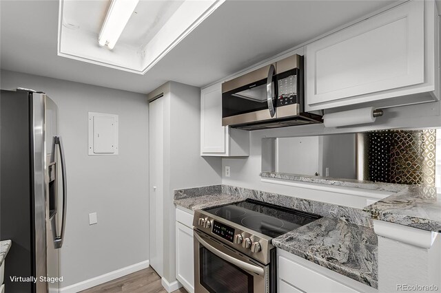 kitchen featuring electric panel, light hardwood / wood-style flooring, light stone counters, white cabinetry, and stainless steel appliances