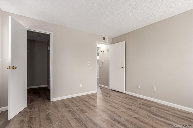 unfurnished bedroom featuring a textured ceiling, a walk in closet, and hardwood / wood-style floors