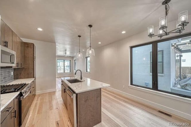 136 Chase St, Salida, CO 81201 - kitchen featuring appliances with stainless steel finishes, light wood finished floors, a center island with sink, brown cabinets, and backsplash