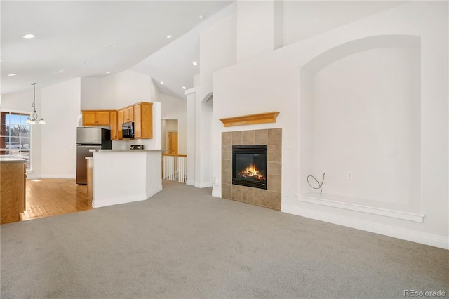 unfurnished living room featuring high vaulted ceiling, a tile fireplace, and light carpet