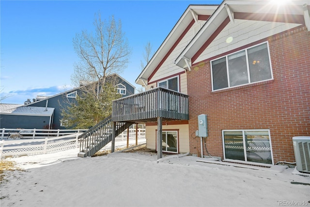 snow covered back of property featuring cooling unit and a wooden deck