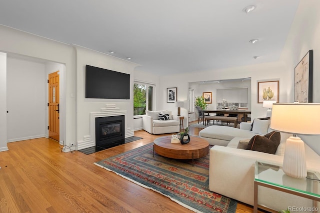 living room featuring a fireplace with flush hearth, wood finished floors, recessed lighting, and baseboards