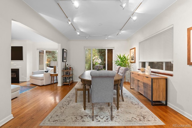 dining area featuring rail lighting, wood finished floors, a glass covered fireplace, and baseboards