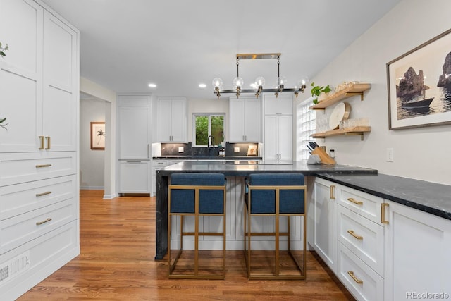 kitchen with white cabinetry, recessed lighting, light wood-style flooring, a kitchen breakfast bar, and a sink