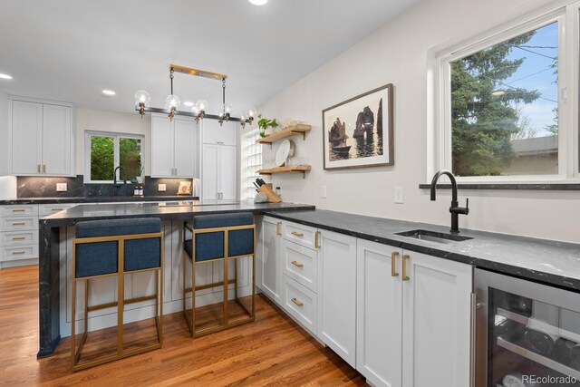 kitchen featuring a sink, beverage cooler, white cabinets, light wood-style flooring, and recessed lighting