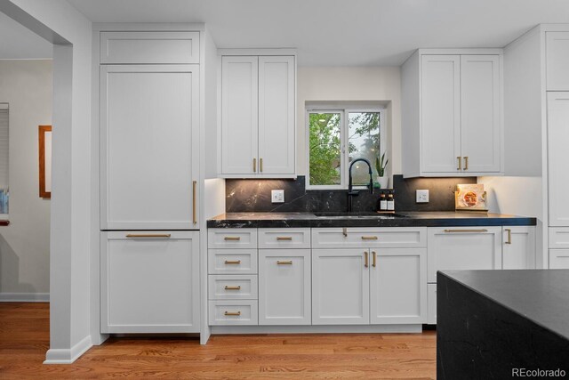 kitchen with a sink, white cabinetry, light wood-type flooring, backsplash, and baseboards