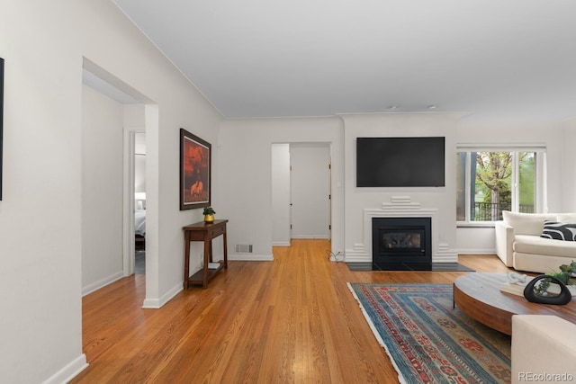 living room featuring light wood-style flooring, a fireplace with flush hearth, and baseboards
