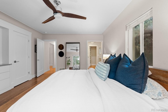 bedroom featuring wood finished floors, ceiling fan, ensuite bath, and baseboards