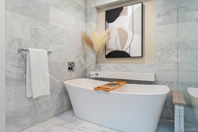 bathroom featuring tile walls, marble finish flooring, and a freestanding tub