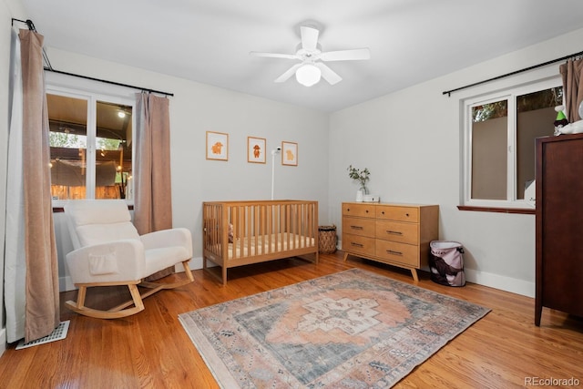 bedroom featuring wood finished floors, a crib, baseboards, and ceiling fan