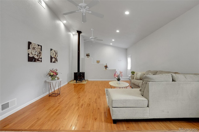 living room with lofted ceiling, ceiling fan, a wood stove, and light hardwood / wood-style flooring