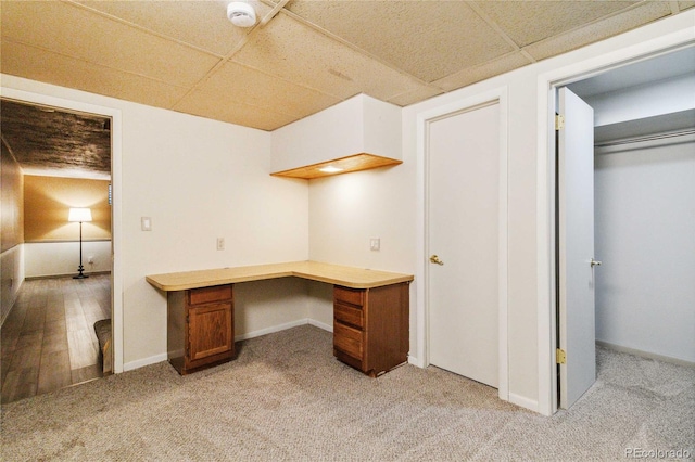 unfurnished office featuring a drop ceiling, light carpet, and built in desk