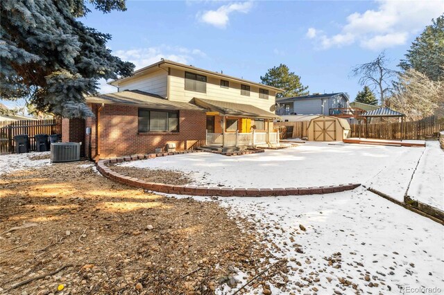 snow covered property with central AC unit and a storage shed