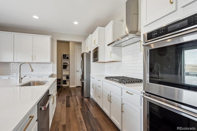 kitchen with light countertops, appliances with stainless steel finishes, white cabinets, a sink, and wall chimney range hood