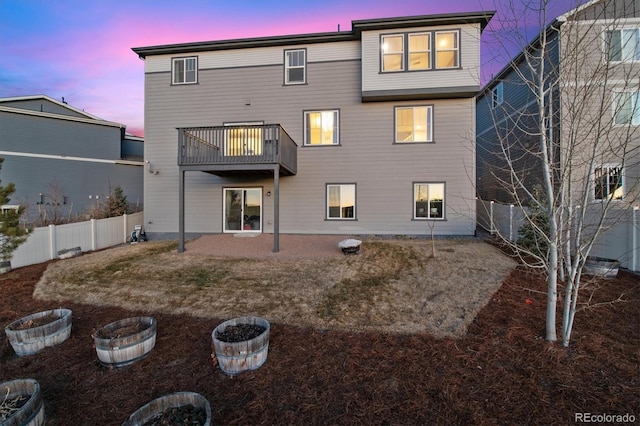 back of property at dusk featuring a fenced backyard and a balcony