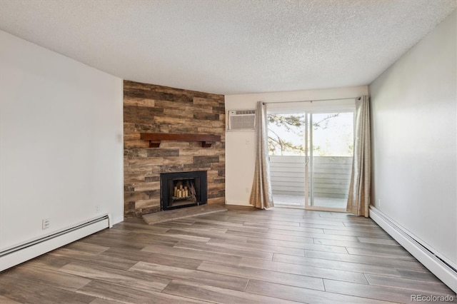 unfurnished living room featuring baseboard heating, wood finished floors, a fireplace, a textured ceiling, and a wall unit AC