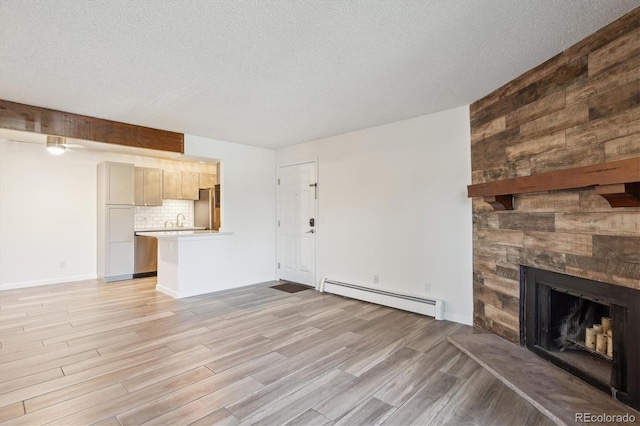 unfurnished living room featuring baseboard heating, light wood-style flooring, a sink, a fireplace, and a textured ceiling