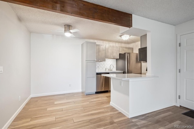 kitchen featuring stainless steel appliances, a textured ceiling, light countertops, light wood-style floors, and tasteful backsplash