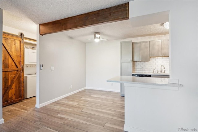 kitchen with stacked washer / drying machine, light countertops, backsplash, light wood-type flooring, and a ceiling fan