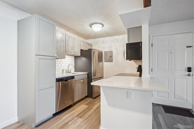 kitchen featuring appliances with stainless steel finishes, light countertops, a textured ceiling, a sink, and light wood finished floors