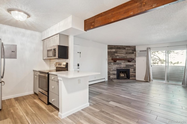 kitchen with appliances with stainless steel finishes, baseboard heating, a textured ceiling, light wood finished floors, and a peninsula