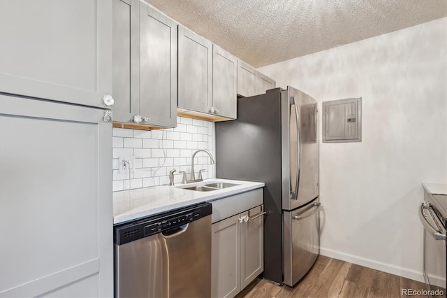 kitchen featuring appliances with stainless steel finishes, a sink, electric panel, wood finished floors, and a textured ceiling