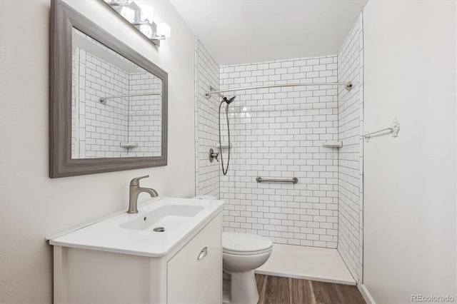 bathroom with wood finished floors, a tile shower, toilet, and vanity