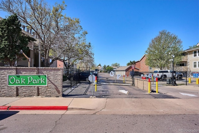 view of asphalt road with a residential view, a gate, a gated entry, street lights, and curbs