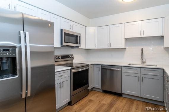 kitchen with appliances with stainless steel finishes, sink, white cabinetry, gray cabinetry, and light hardwood / wood-style floors