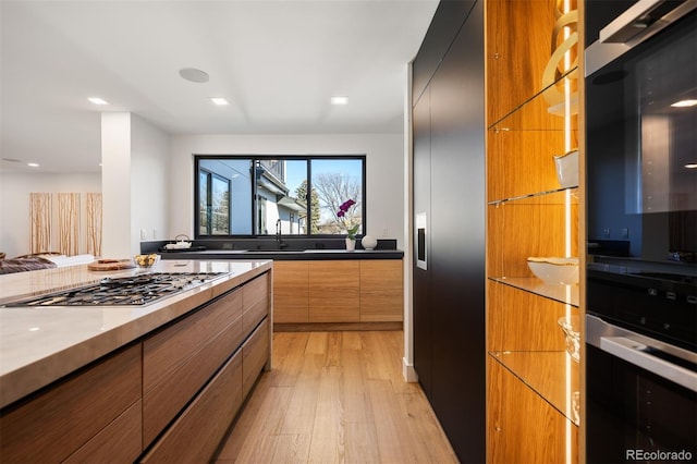 kitchen featuring modern cabinets, brown cabinets, light wood-style floors, stainless steel gas cooktop, and a sink