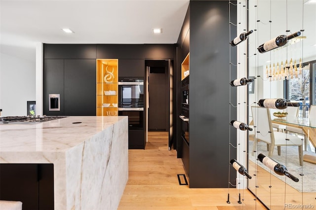 kitchen with dark cabinets, stainless steel gas cooktop, dobule oven black, light wood-type flooring, and modern cabinets