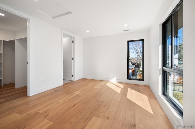 unfurnished bedroom with attic access, light wood-type flooring, a spacious closet, and baseboards