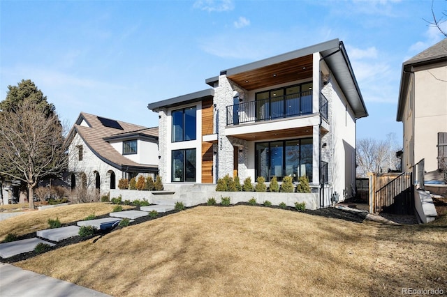 rear view of house featuring stone siding, a lawn, a balcony, and stucco siding