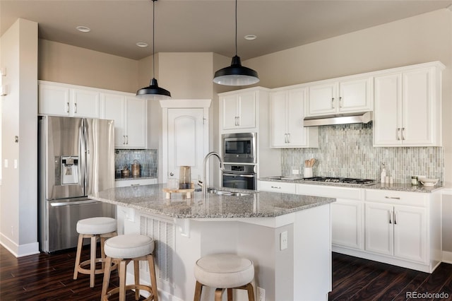 kitchen with appliances with stainless steel finishes, an island with sink, white cabinetry, and light stone countertops