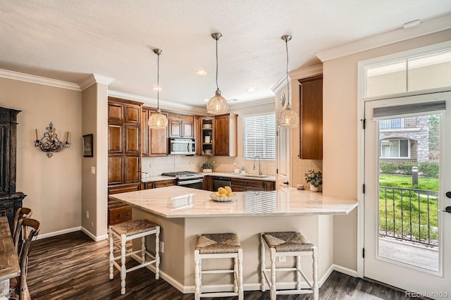 kitchen with dark wood-style flooring, appliances with stainless steel finishes, a sink, a breakfast bar area, and a peninsula