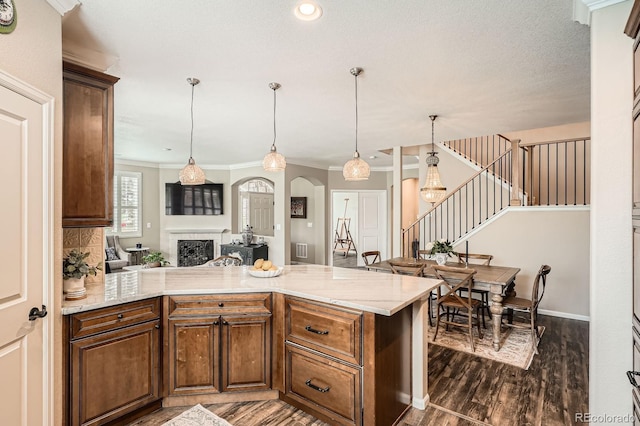 kitchen with ornamental molding, dark wood-style flooring, a peninsula, light stone counters, and arched walkways