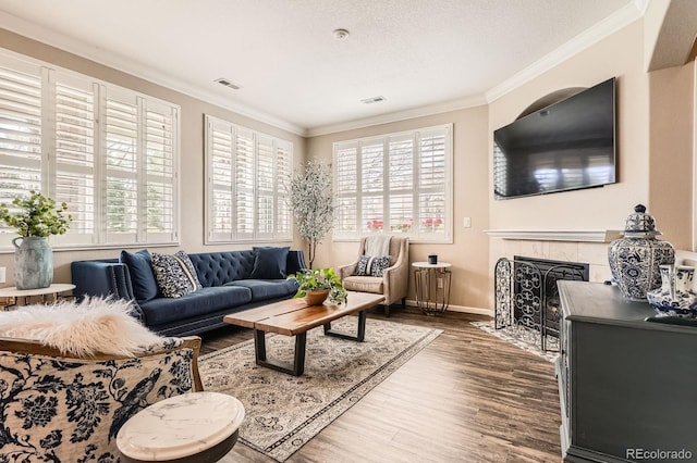 living room featuring crown molding, wood finished floors, visible vents, and a tile fireplace